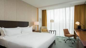 A hotel room with a large bed, a desk with a chair, a lamp, and a window with curtains.