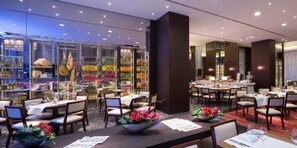 A restaurant with multiple tables and chairs, a glass display case with food items, and a view of the cityscape. - Hilton Kyiv (Kyiv)