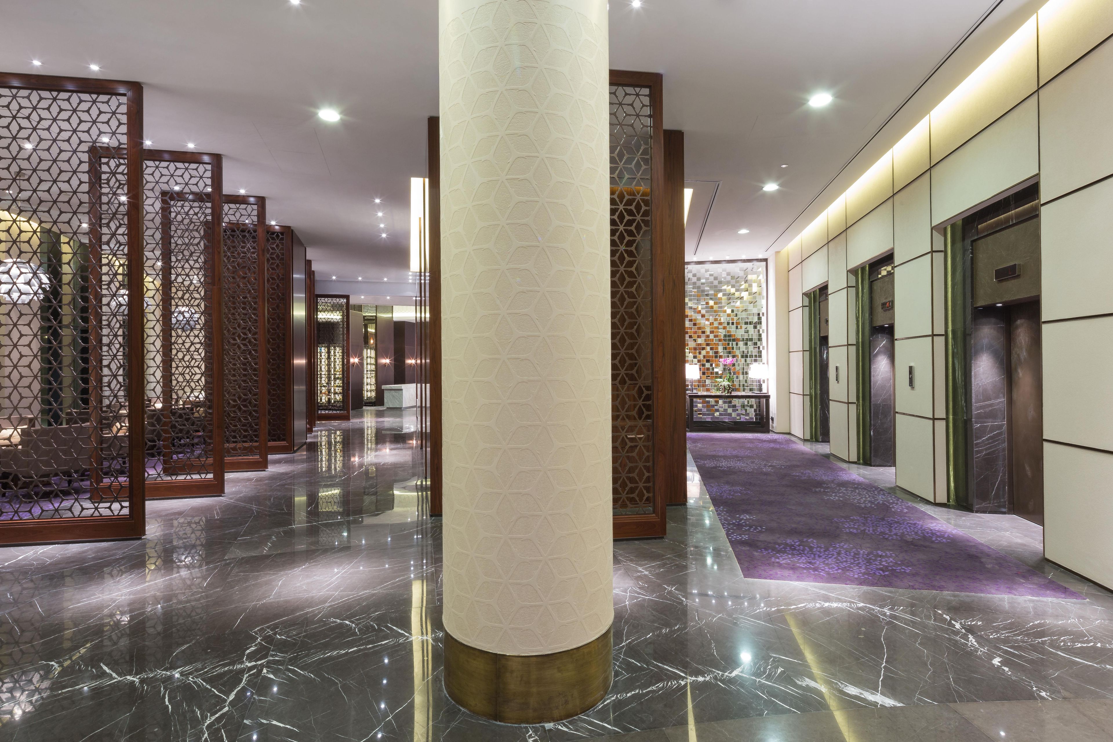 Un hall de hotel con suelo de mármol, separadores de madera y una zona de recepción con un papel tapiz estampado.