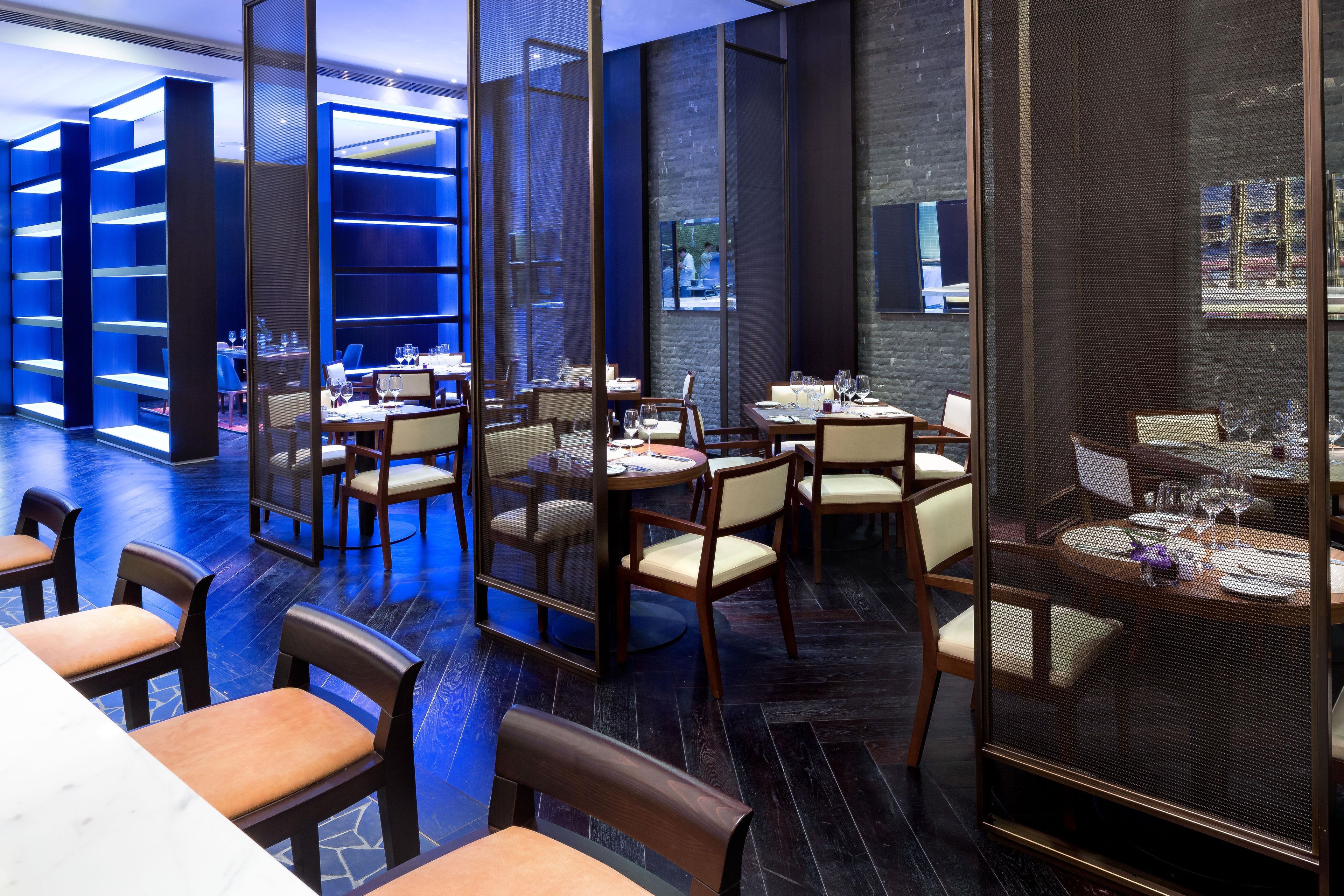 Un restaurant moderne, doté d’un intérieur éclairé de lumière bleue, de meubles en bois et offrant une vue à travers un écran ajouré.