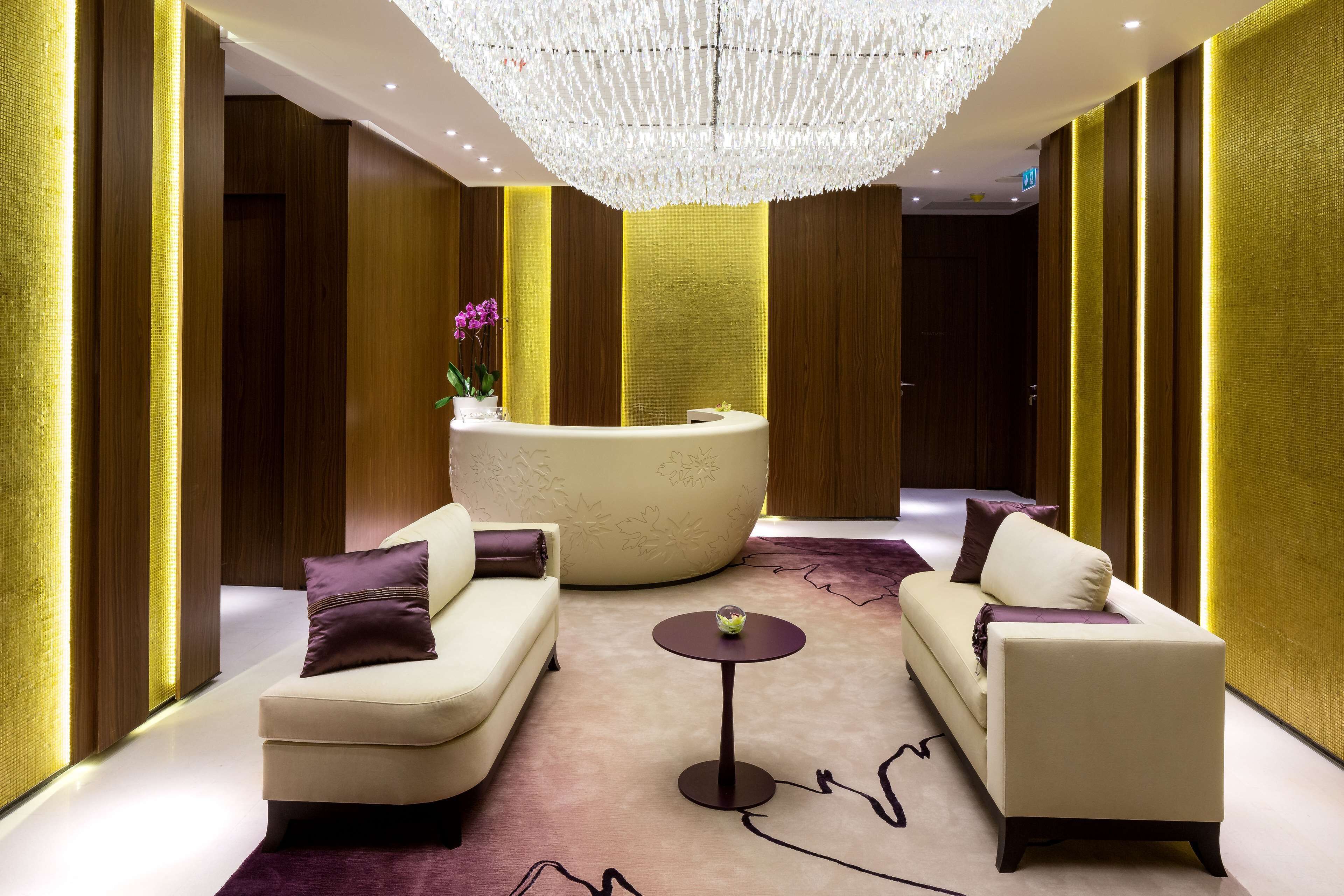 A reception area with a curved reception desk, two sofas, a small round table, and a chandelier.