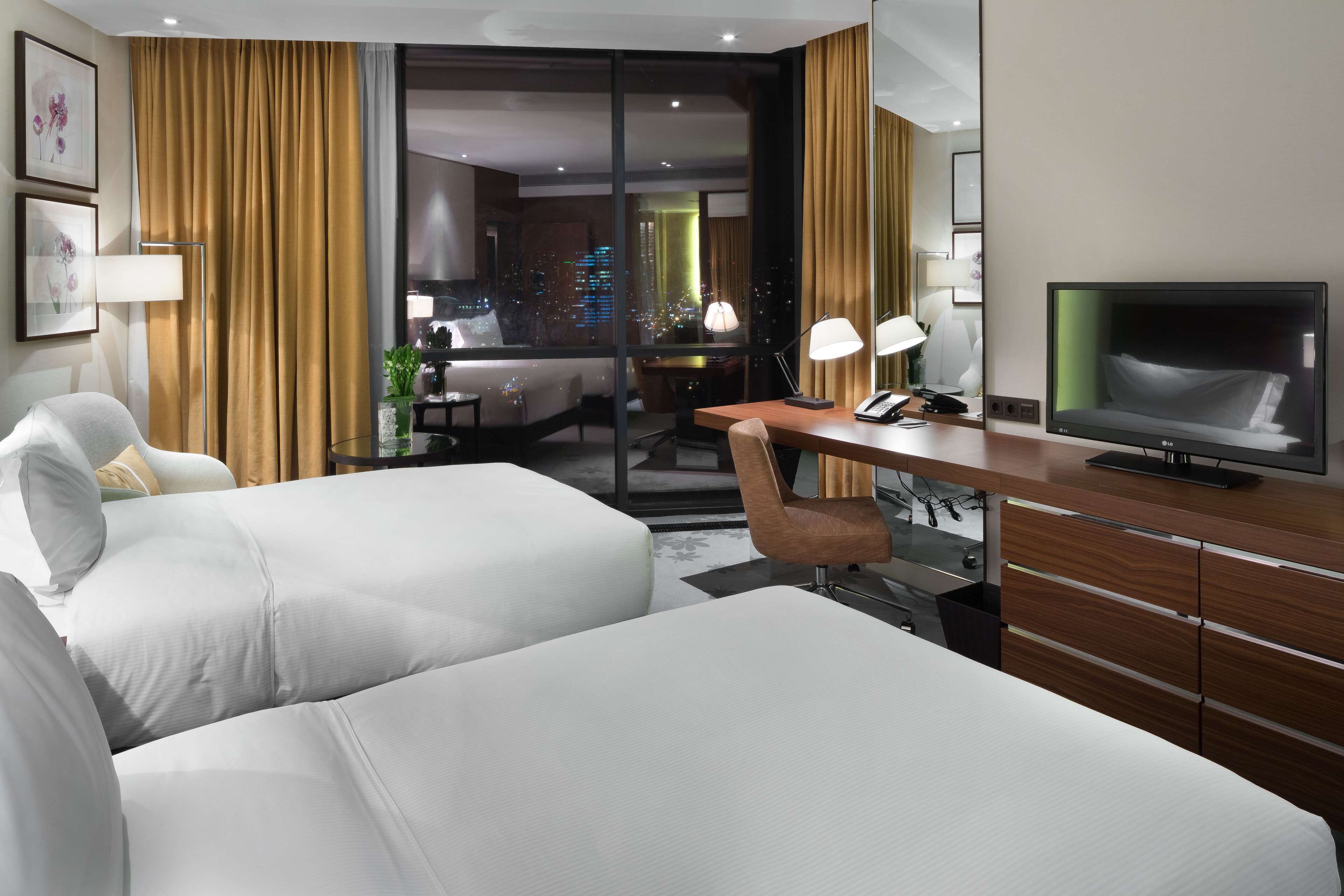 Une chambre d’hôtel avec deux lits, un bureau avec une télévision, une chaise et une vue sur le paysage urbain par la fenêtre.