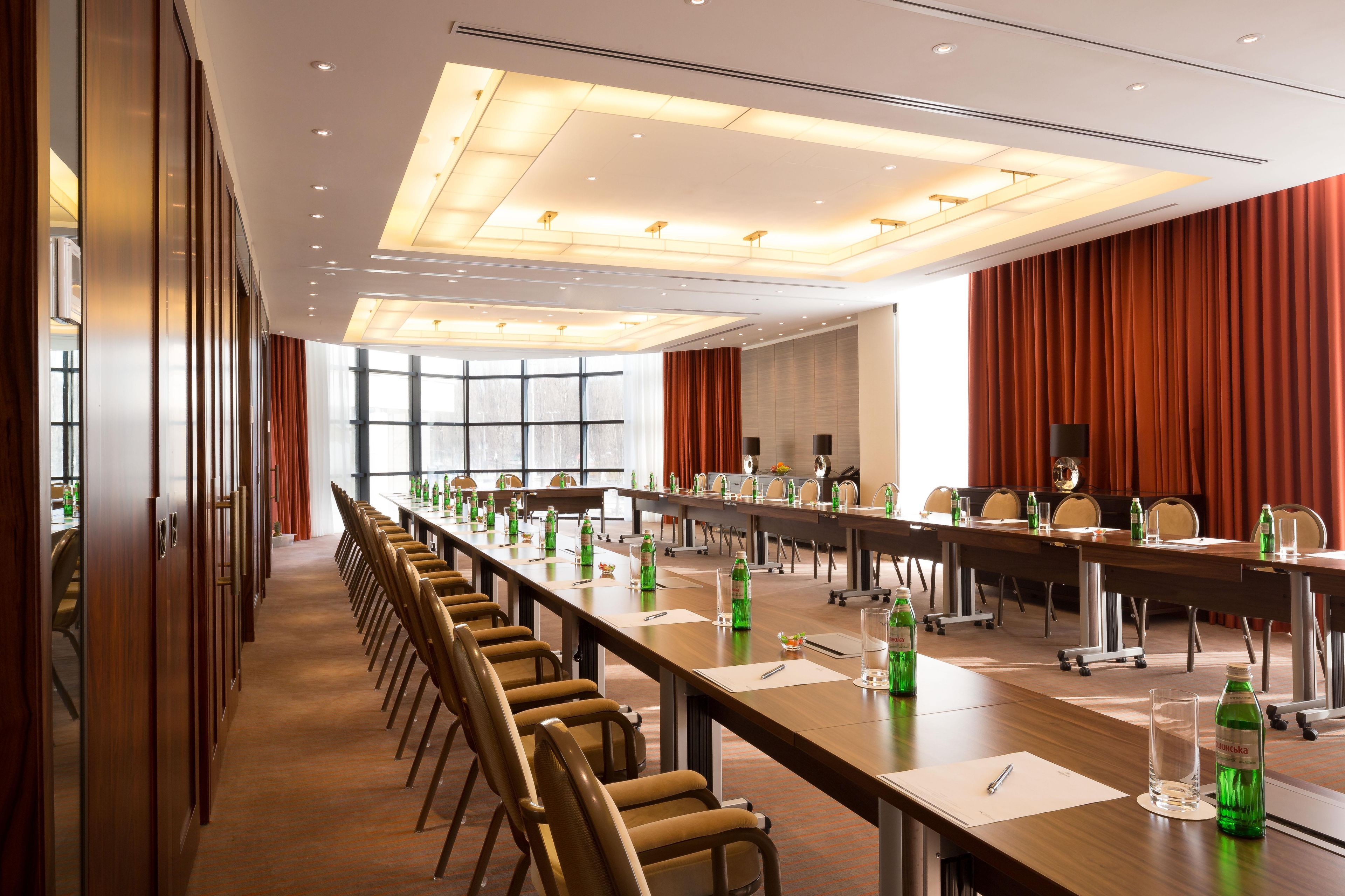 Sala de conferência com mesas compridas, cadeiras e garrafas de água.