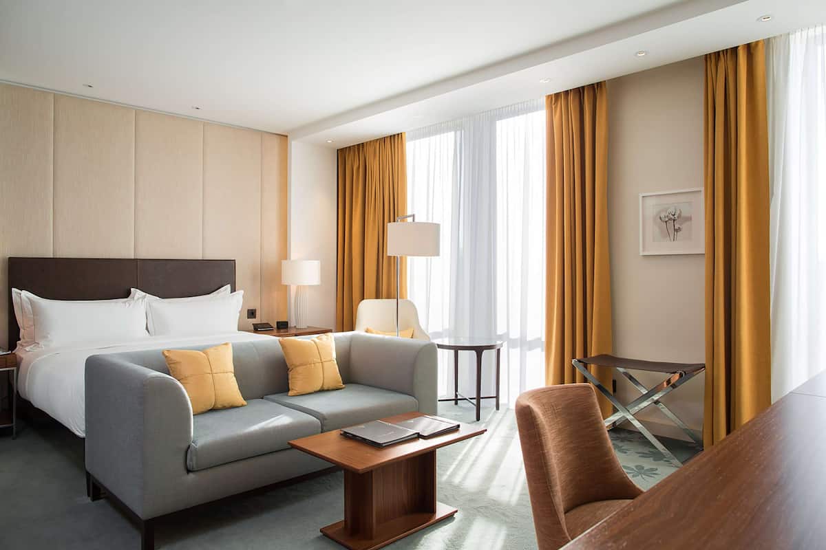 Ett hotellrum med en säng, soffa, fåtölj, soffbord, lampa och ett litet bord.