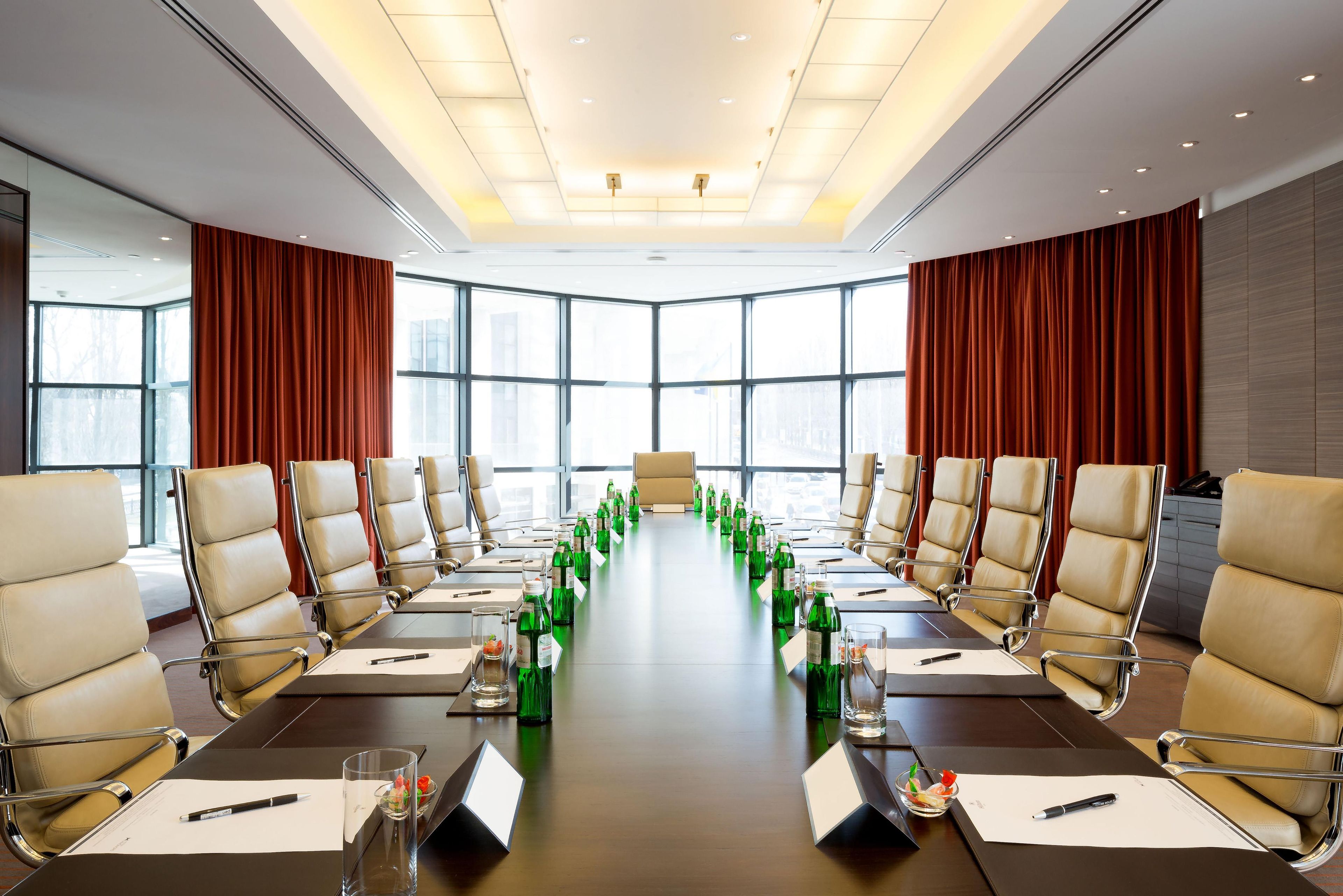 Un salón de conferencias con una larga mesa, sillas y botellas verdes.