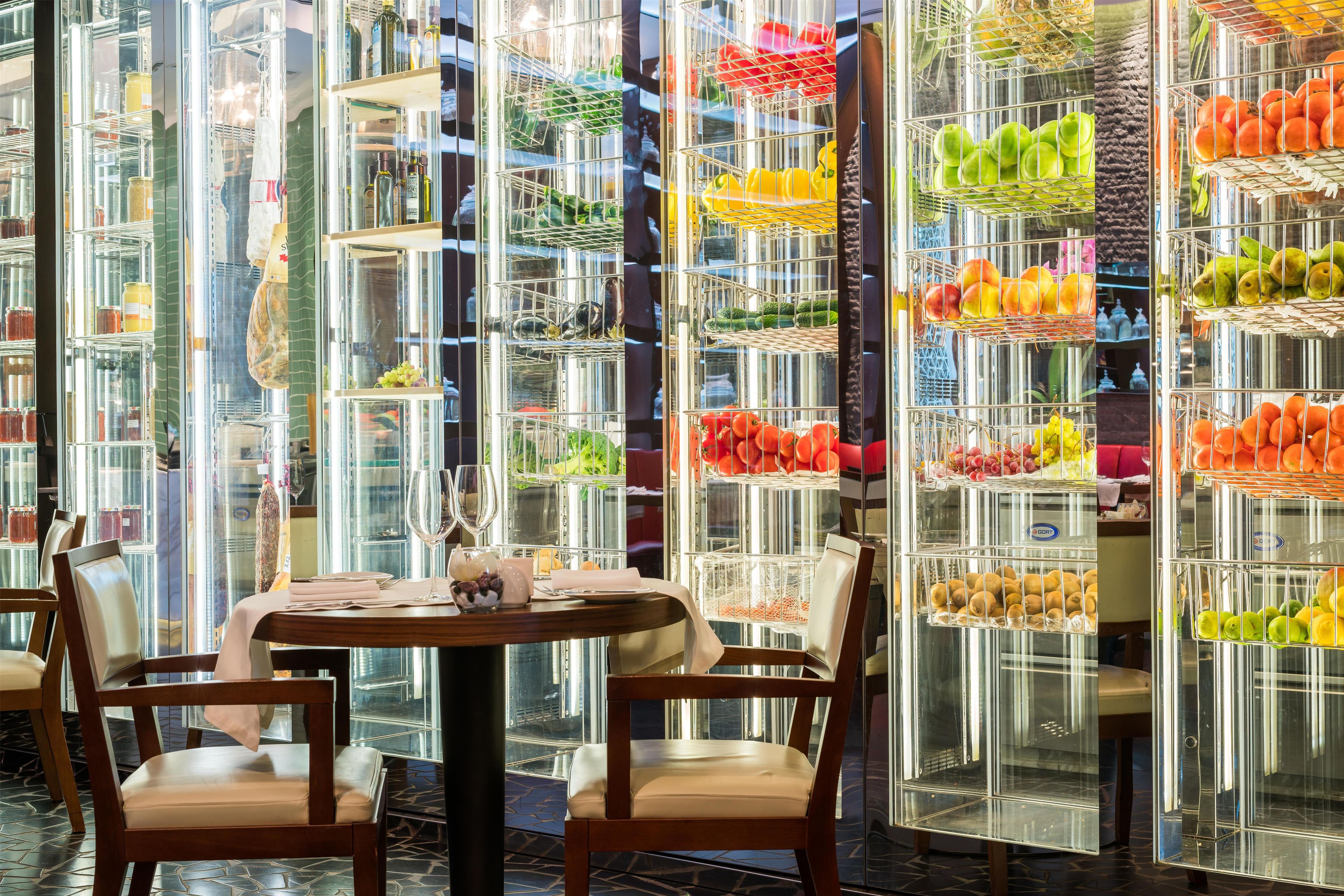 Ein Restaurantinneres mit einer Glastheke voller Obst und Gemüse, Holzsessel und ein für das Essen gedeckter Tisch.