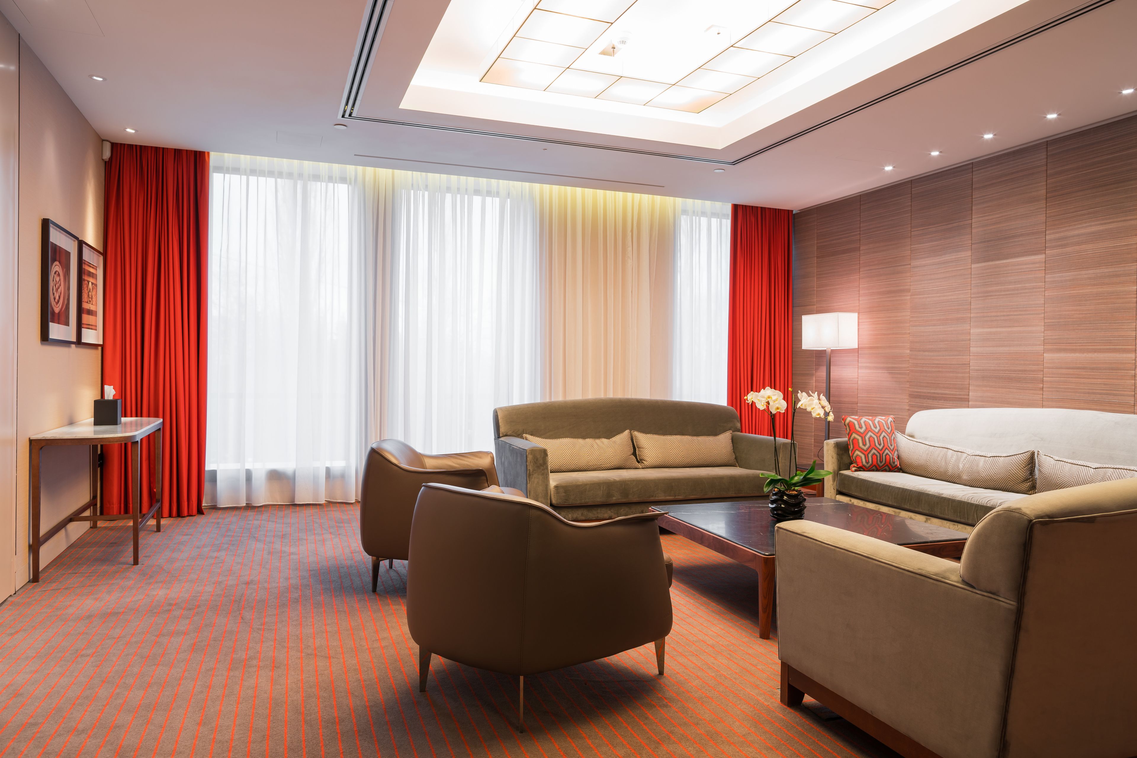 A modern hotel room with a sofa, armchairs, a small table, and a lamp.