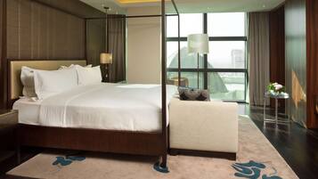 A modern hotel room with a large bed, a sitting area, and a view of the city through large windows.