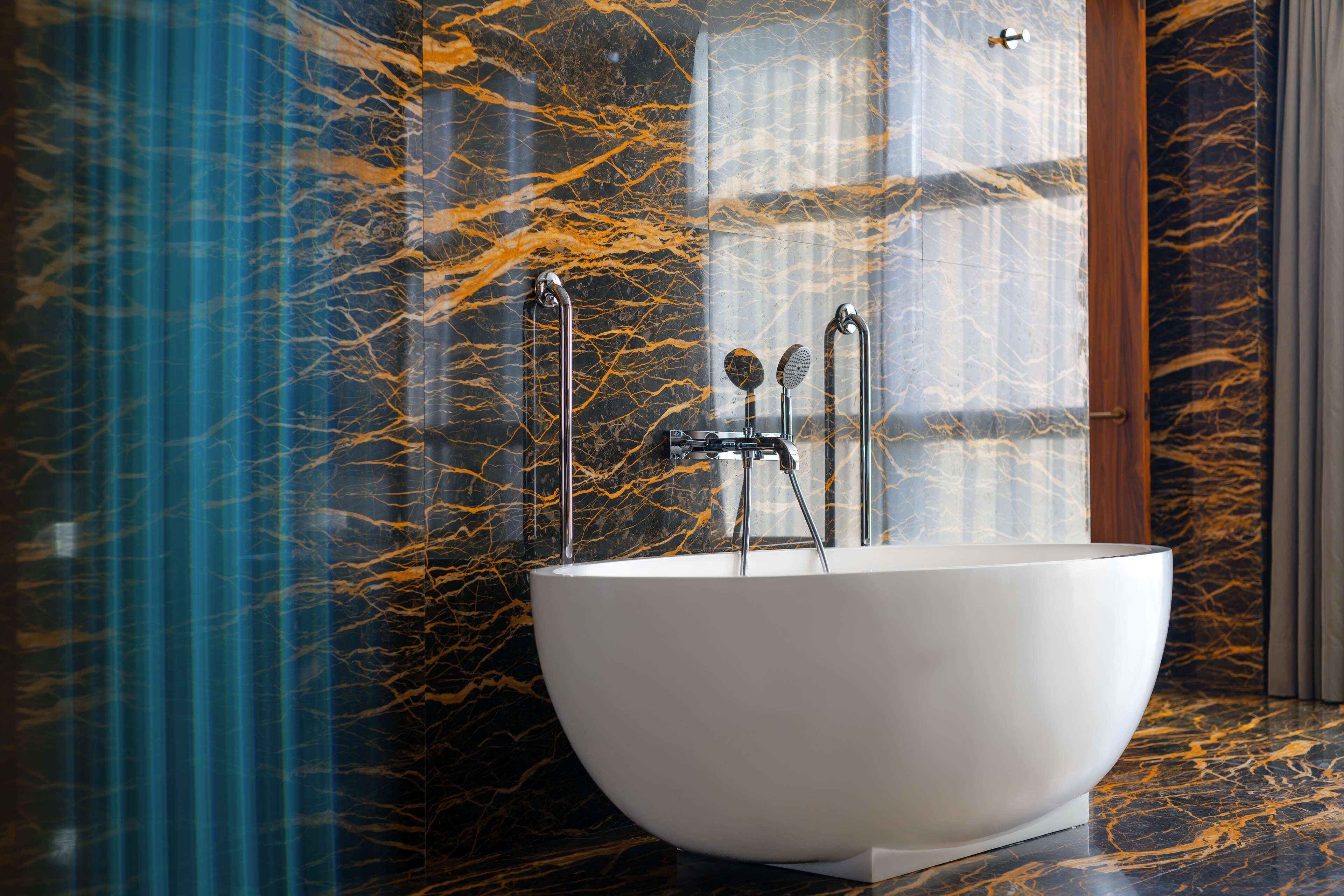 A modern bathroom with a freestanding bathtub, marble walls, and a glass shower enclosure.