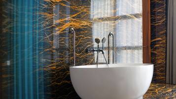 A modern bathroom with a freestanding bathtub, marble walls, and a glass shower enclosure.