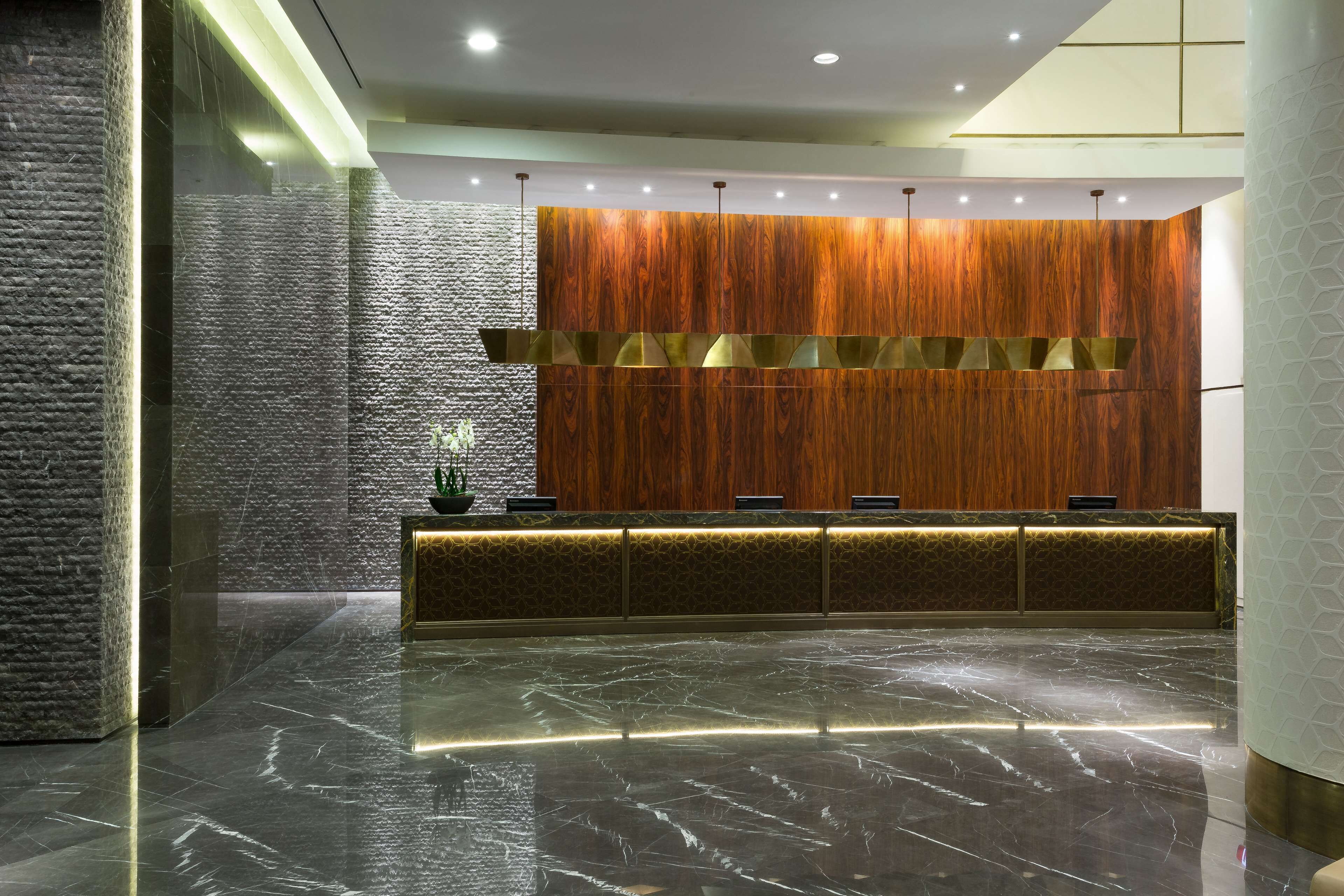 Zona de recepción con pared de paneles de madera, piso de mármol y un mostrador con diseño decorativo.