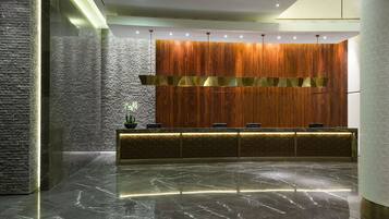 Zona de recepción con pared de paneles de madera, piso de mármol y un mostrador con diseño decorativo.