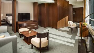 Ein modernes Hotelzimmer mit einem großen Bett, einem Schreibtisch mit Flachbildfernseher, einer Sitzecke mit Sofa und Sesseln sowie einem Holzschrank.