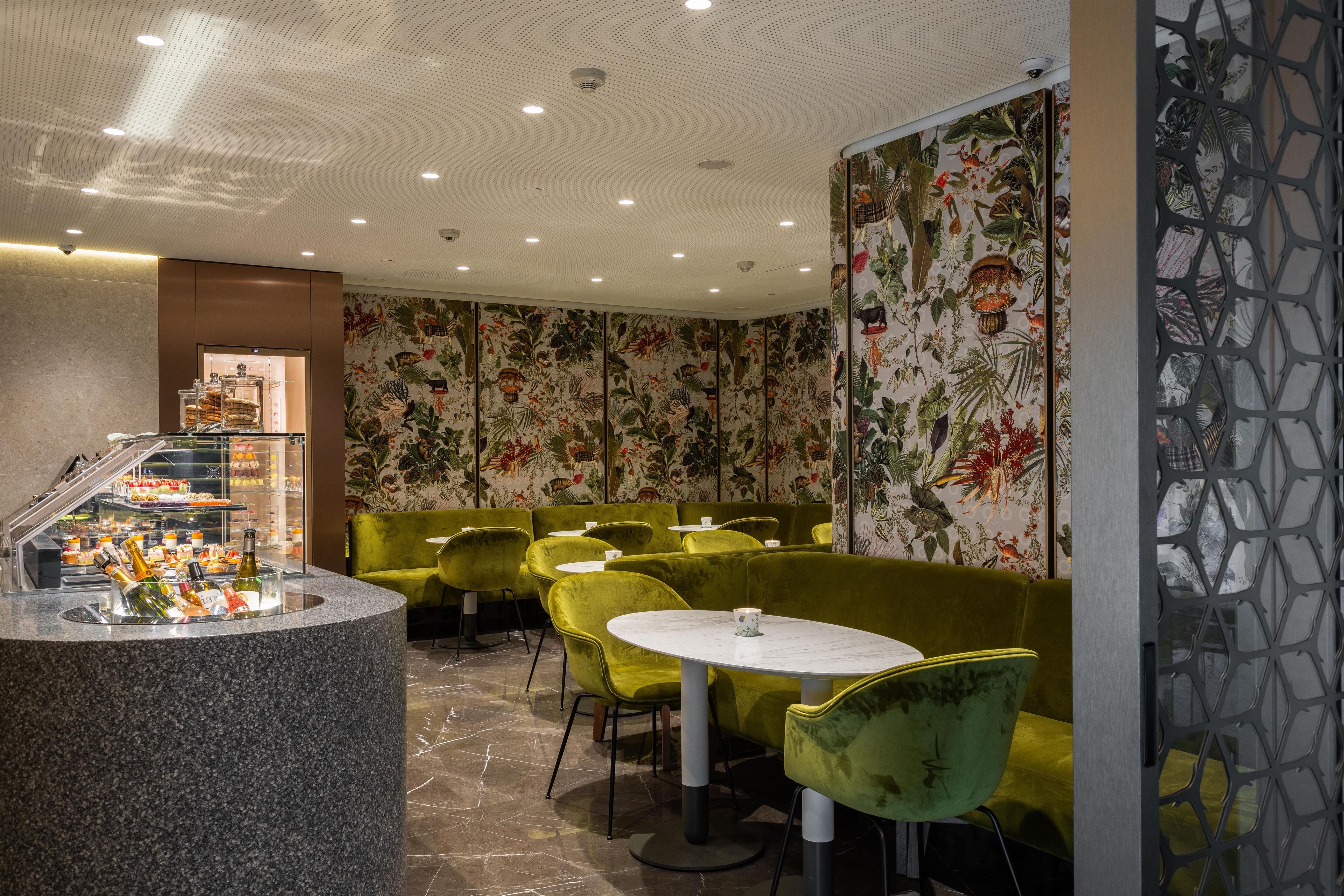 A restaurant interior with a bar area, green upholstered seating, and a floral wallpaper design.