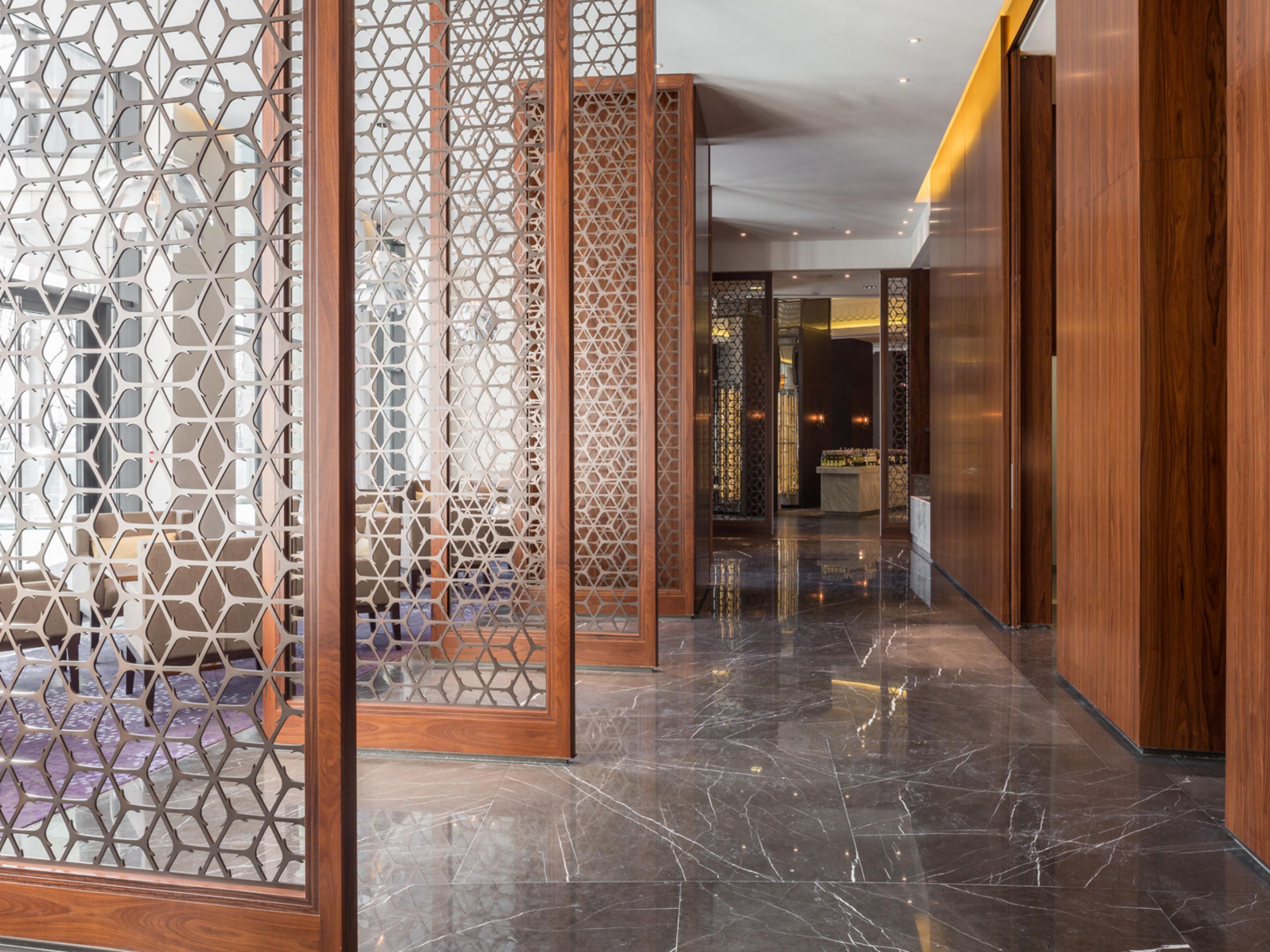 A corridor with a polished marble floor, wooden paneling, and a view into a bar area.