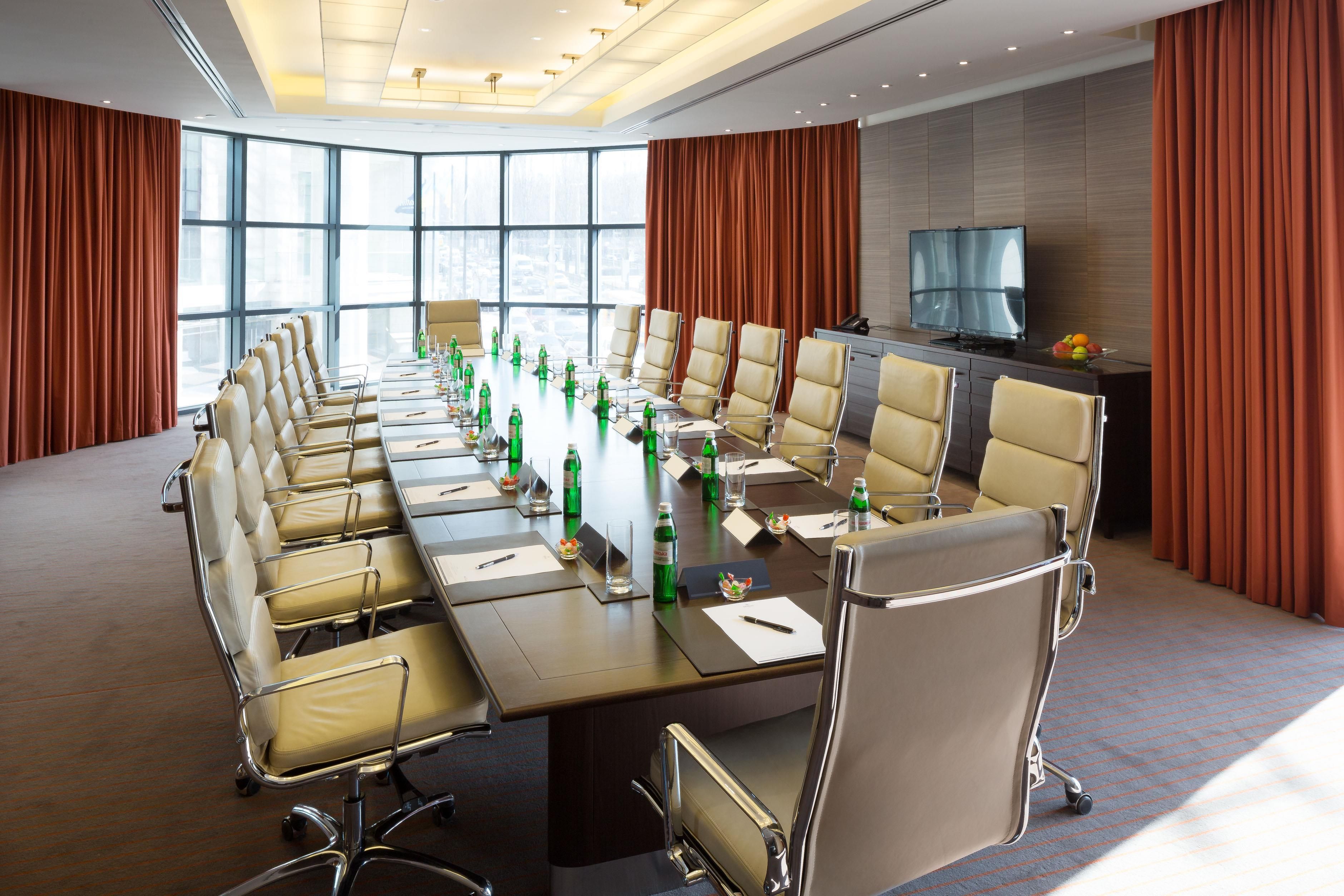 Une salle de conférence avec une longue table, des chaises et un téléviseur.