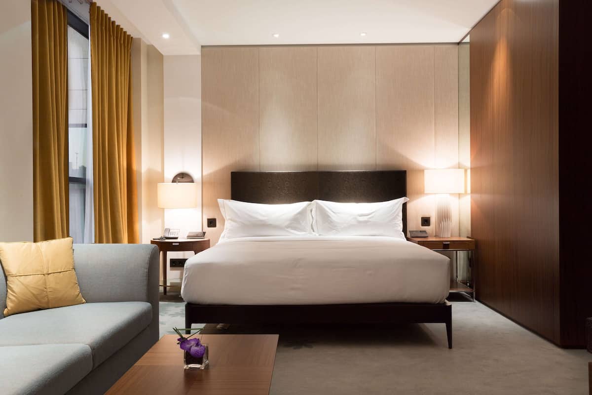Ett hotellrum med en stor säng, en soffa, två sängbord med lampor och en sänggavel i trä.