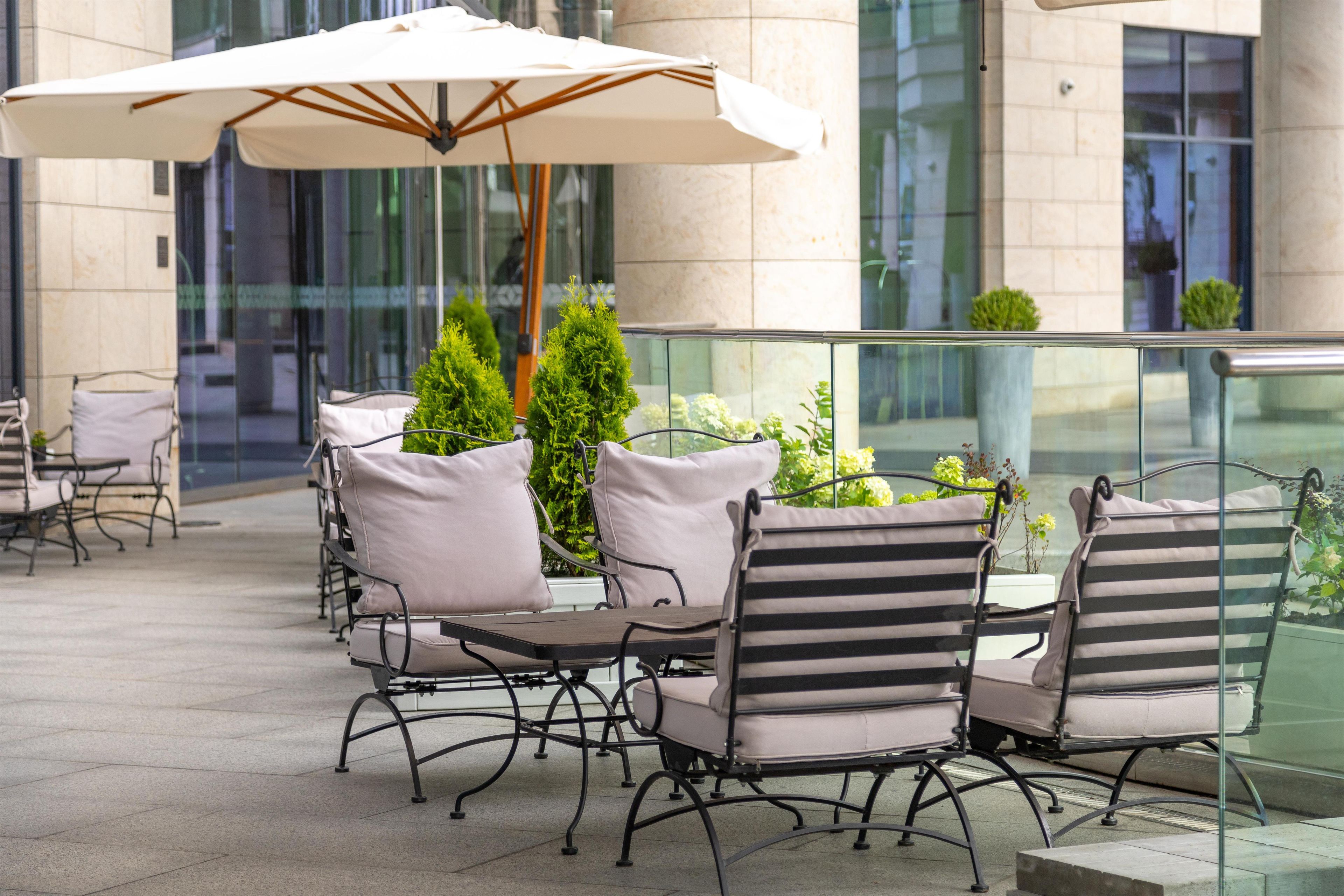An outdoor seating area with tables and chairs, an umbrella, and potted plants.