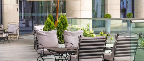 An outdoor seating area with tables and chairs, an umbrella, and potted plants.