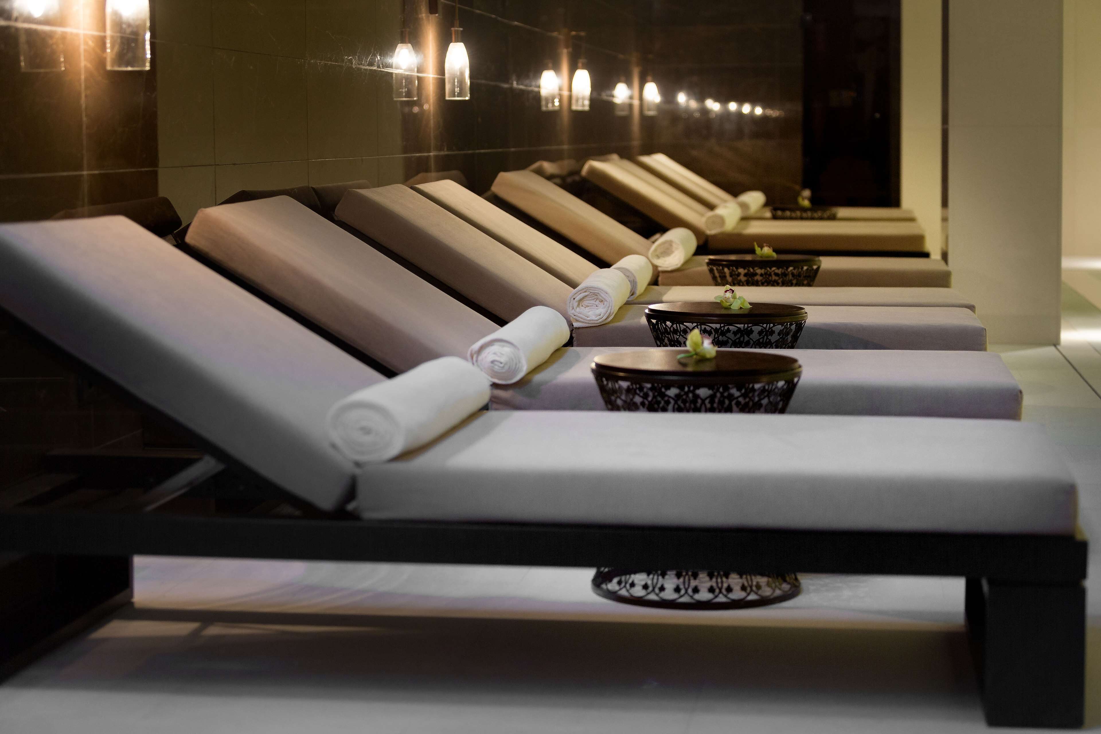 A row of sun loungers with towels neatly rolled up, each accompanied by a small table with a decorative bowl.