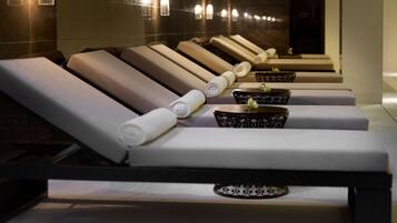 A row of sun loungers with towels neatly rolled up, each accompanied by a small table with a decorative bowl.