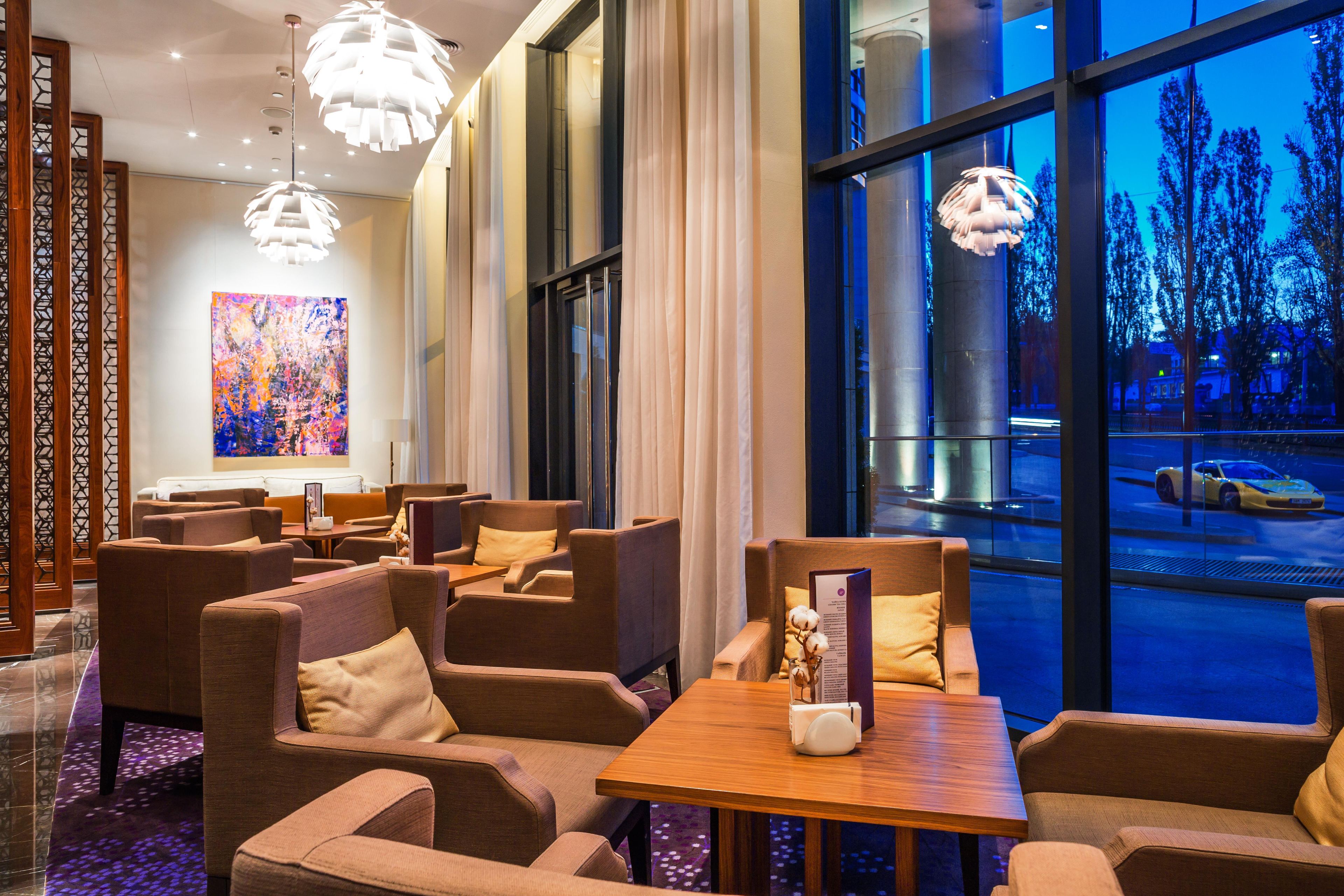 A modern hotel lobby with seating areas, large windows, and decorative lighting.
