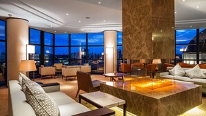 A modern hotel lobby with a large, central fire feature, comfortable seating, and large windows offering a city view. - Hilton Kyiv (Kyiv)