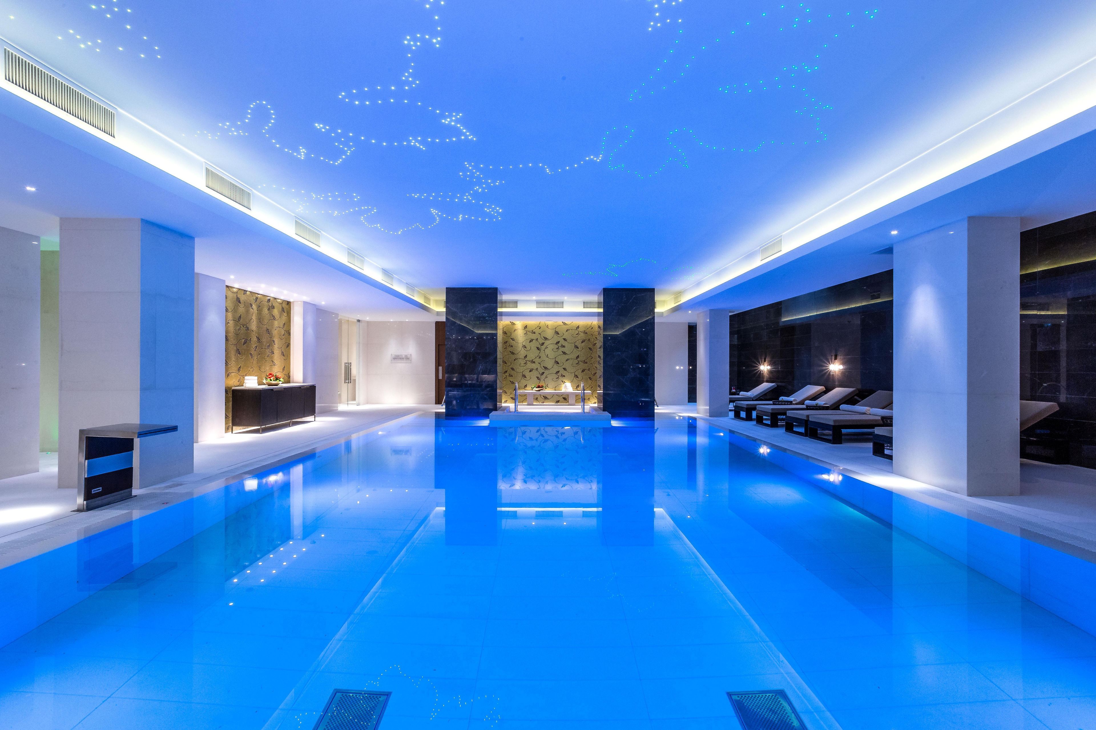 Una piscina interior moderna con una fuente central, zonas de descanso a ambos lados y un muro estampado al fondo.