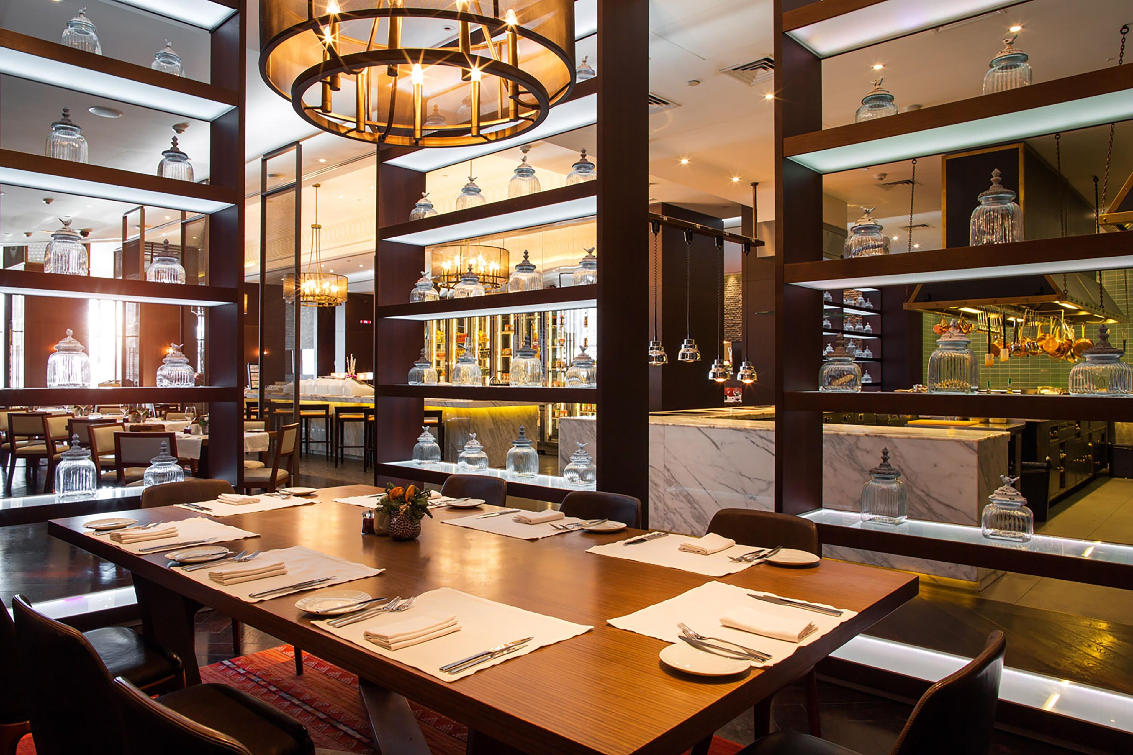A restaurant with a long wooden table set for dining, surrounded by chairs.