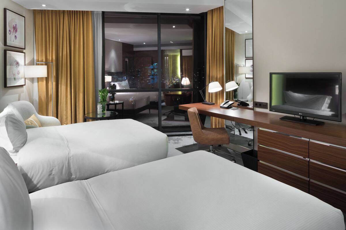 Ett hotellrum med två sängar, ett skrivbord, en TV och utsikt över staden.