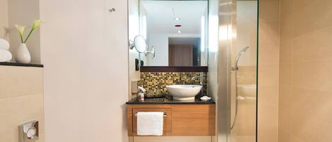 Un baño moderno con ducha envuelta en vidrio, un lavamanos blanco y un mueble de tocador de madera.