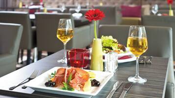 A dining table with a plate of food, two glasses of wine, and a vase with a red flower.