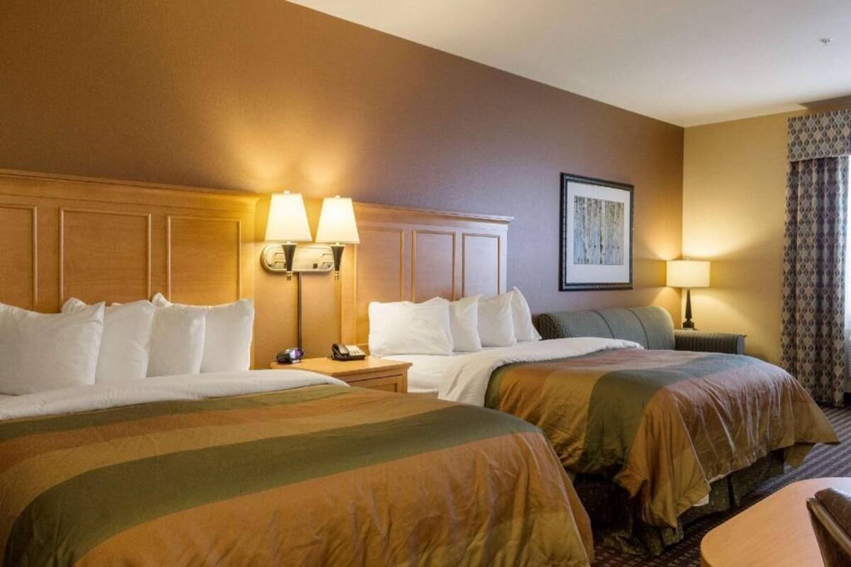 A hotel room with two beds, a headboard, bedside lamps, a nightstand, a framed picture on the wall, and a window with curtains.