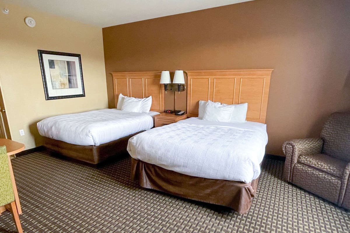 A hotel room with two beds, a wooden headboard, a small table, and a chair.