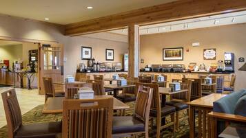 A hotel dining area with wooden tables and chairs, a buffet line, and a kitchen in the background.
