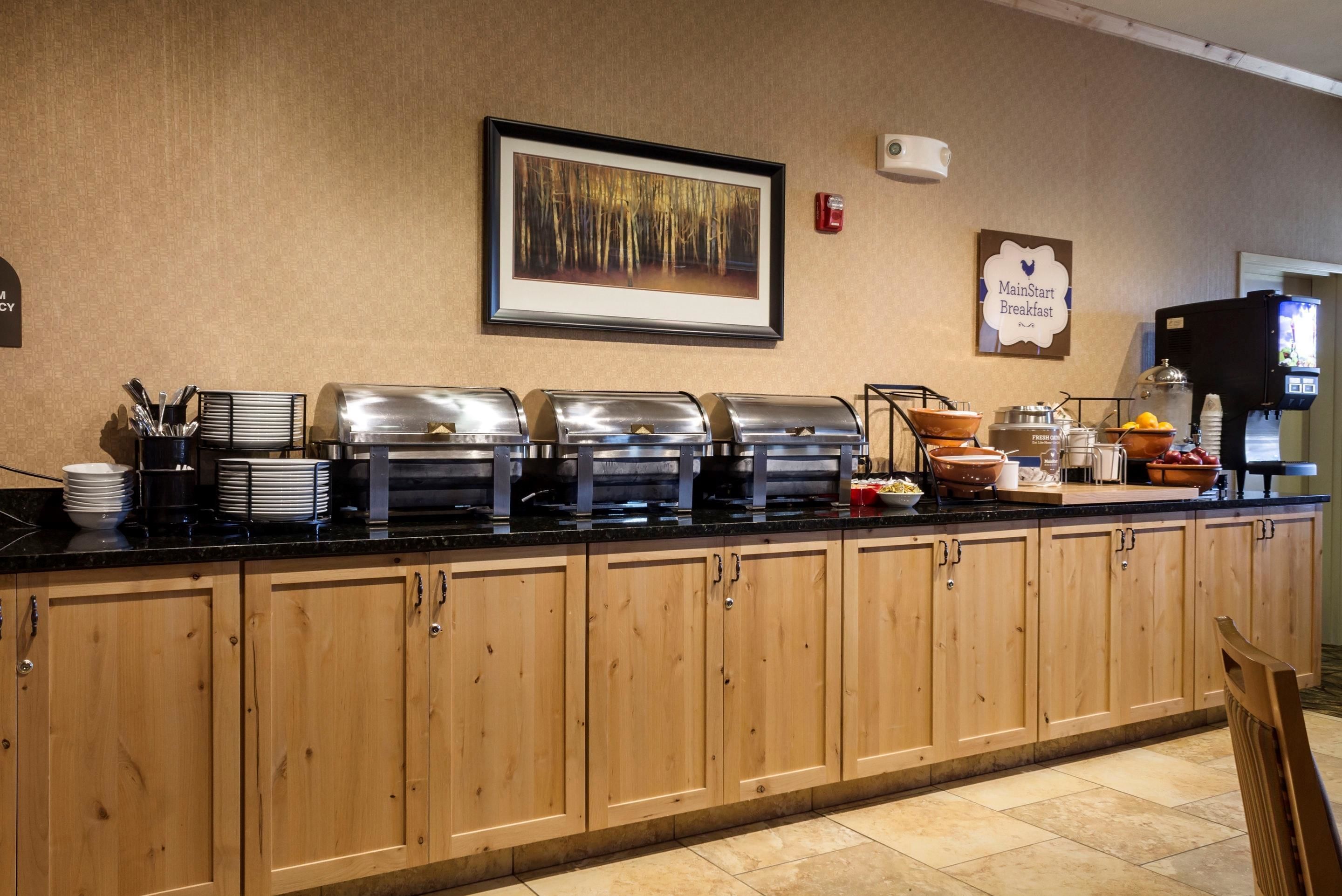 A buffet counter with various food stations, a framed picture on the wall, and a sign indicating the breakfast area.