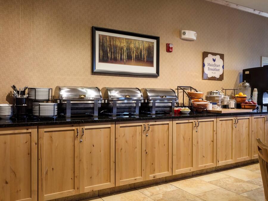 A buffet counter with various food stations, a framed picture on the wall, and a sign indicating the breakfast area.