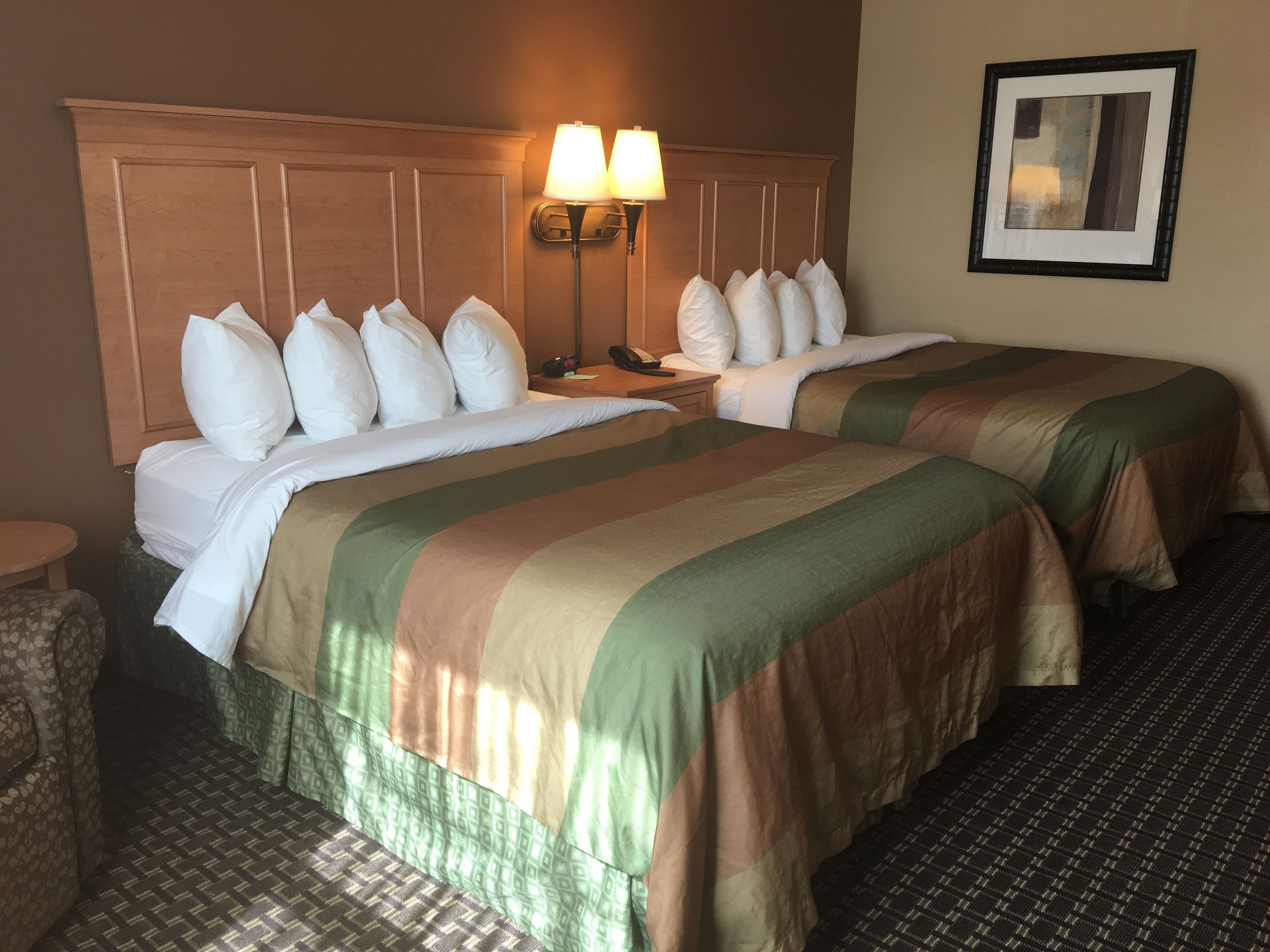 A hotel room with two beds, a nightstand, a lamp, and a framed picture on the wall.