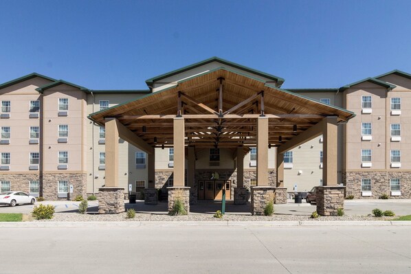 A hotel entrance with a covered walkway, stone pillars, and a parking area. - MainStay Suites Williston (Williston)