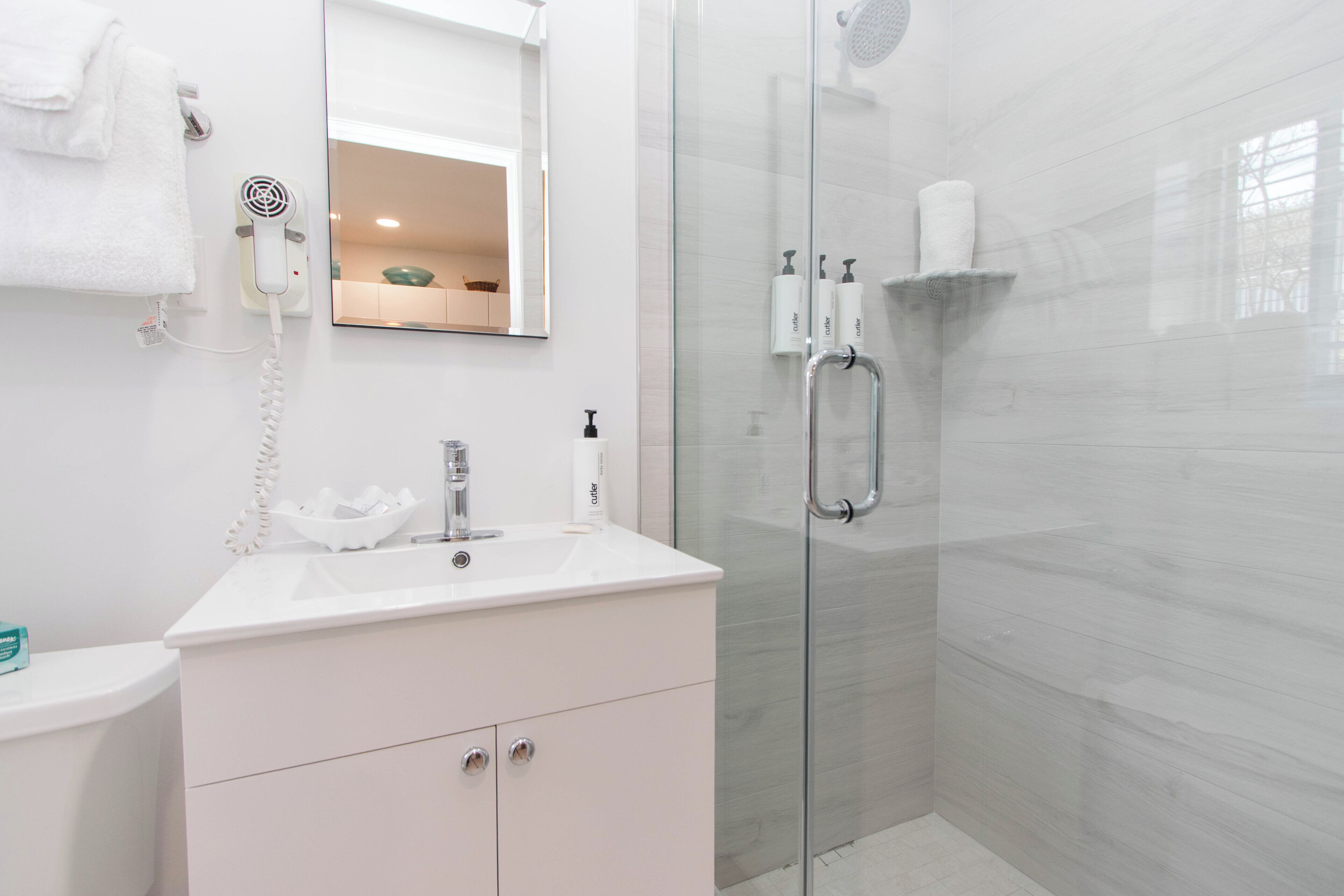 Un bany modern amb un plat de dutxa de vidre, un lavabo blanc i un mirall a sobre.