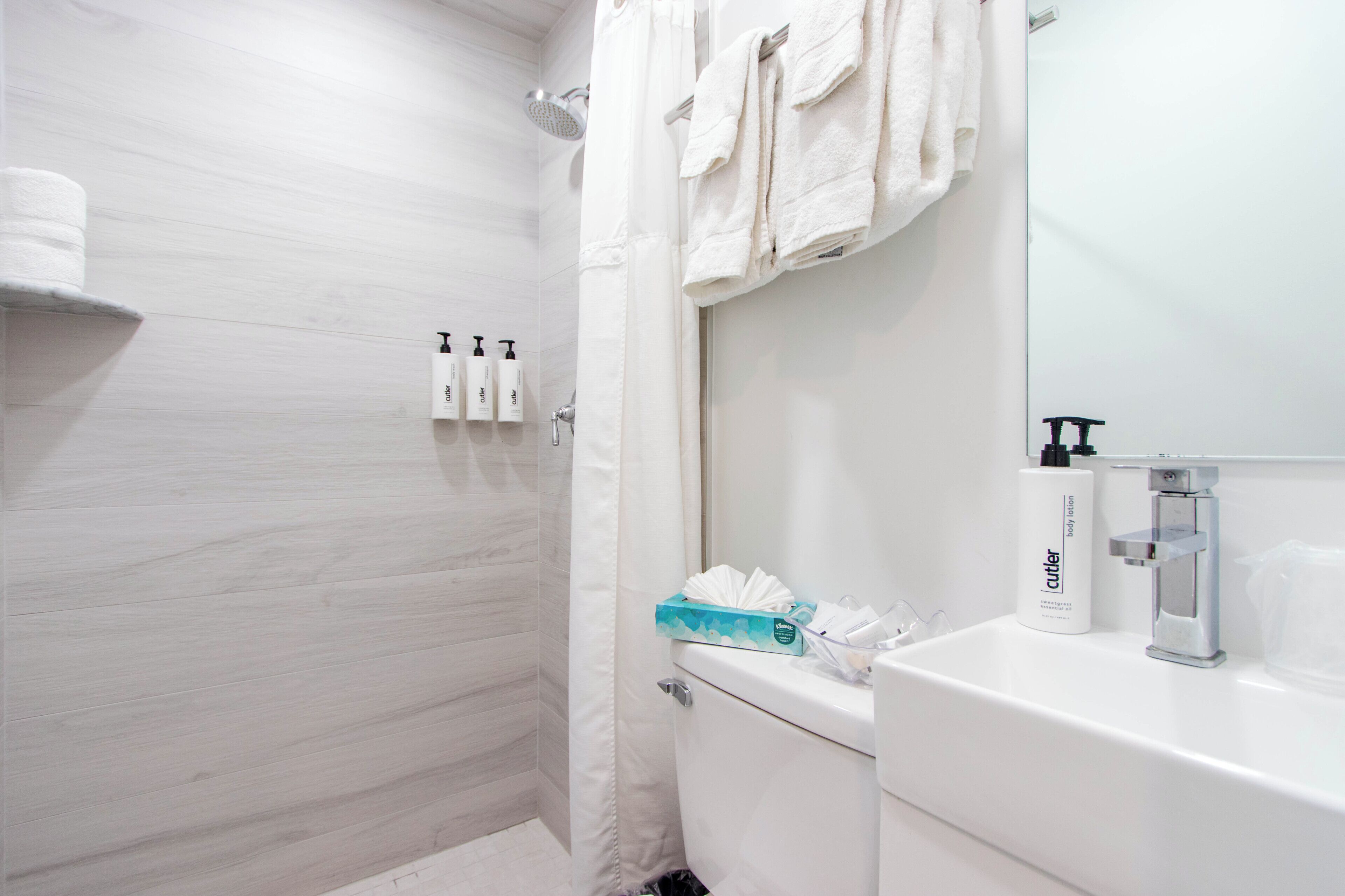 Un baño con ducha, inodoro, lavamanos y barra para toallas.