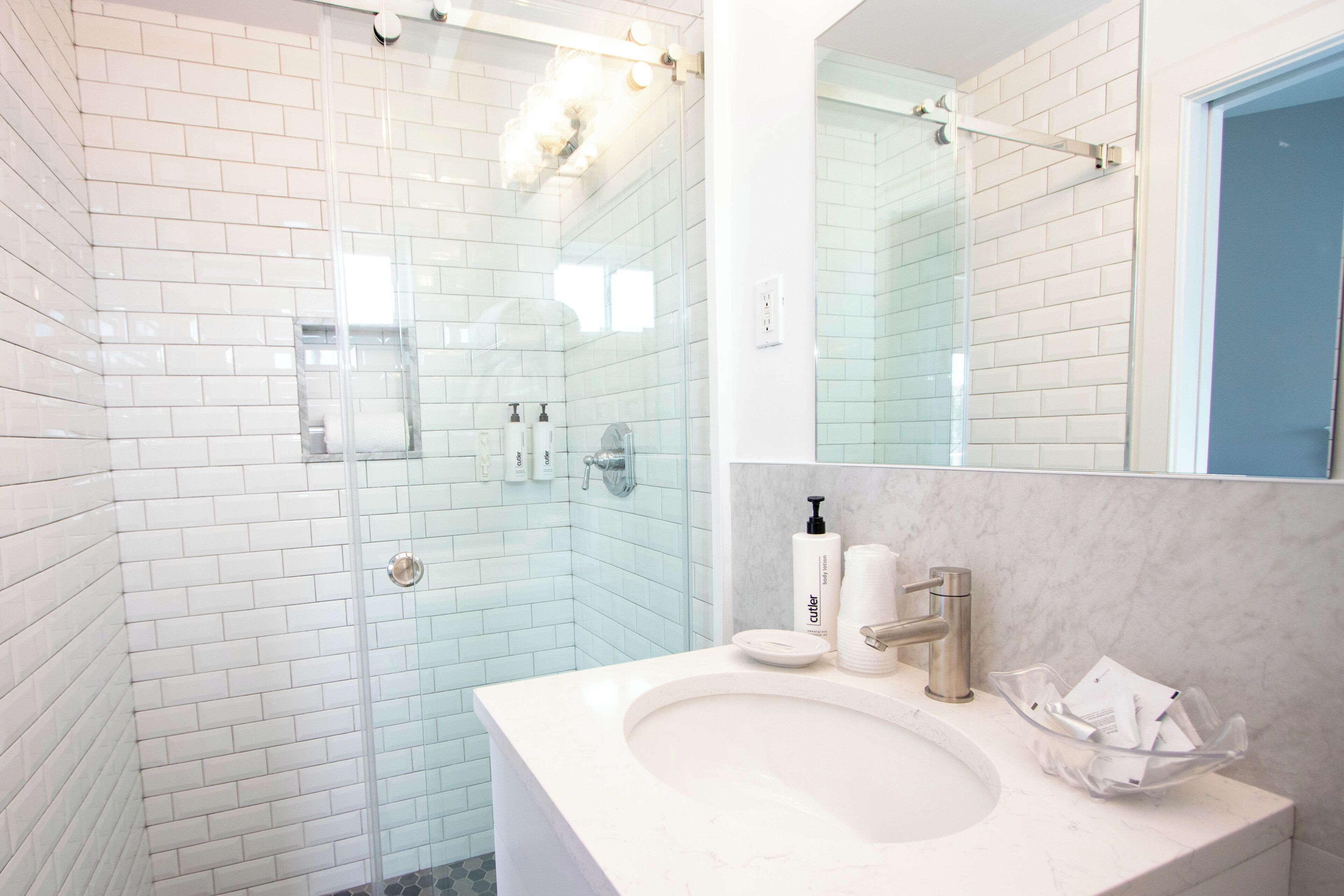 A bathroom with white subway tiles, a glass shower enclosure, a white sink with a marble countertop, and a large mirror.