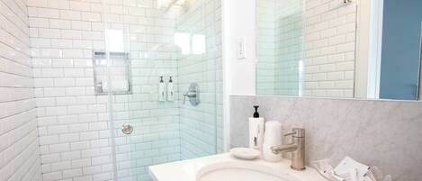 A bathroom with white subway tiles, a glass shower enclosure, a white sink with a marble countertop, and a large mirror.