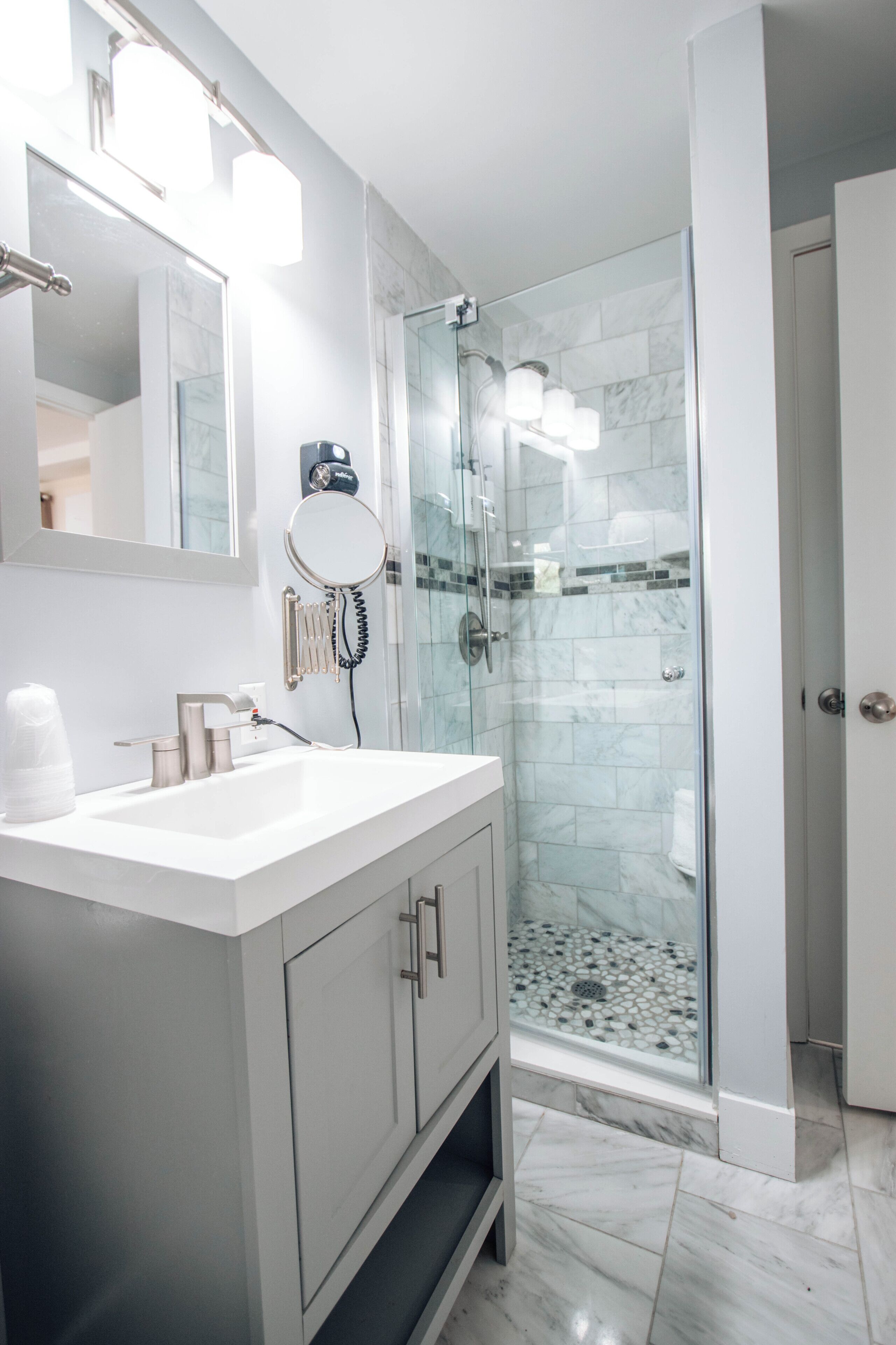 Un bagno moderno con doccia vetrata, un mobile lavabo bianco con specchio e pavimento in marmo.
