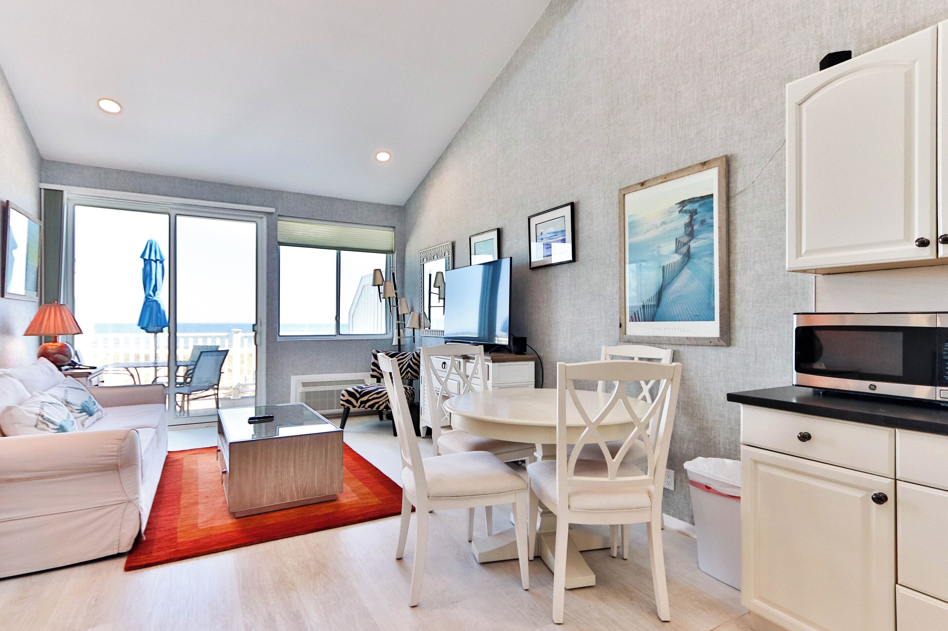A modern living room with a sofa, dining table, chairs, a TV, and artwork on the wall.
