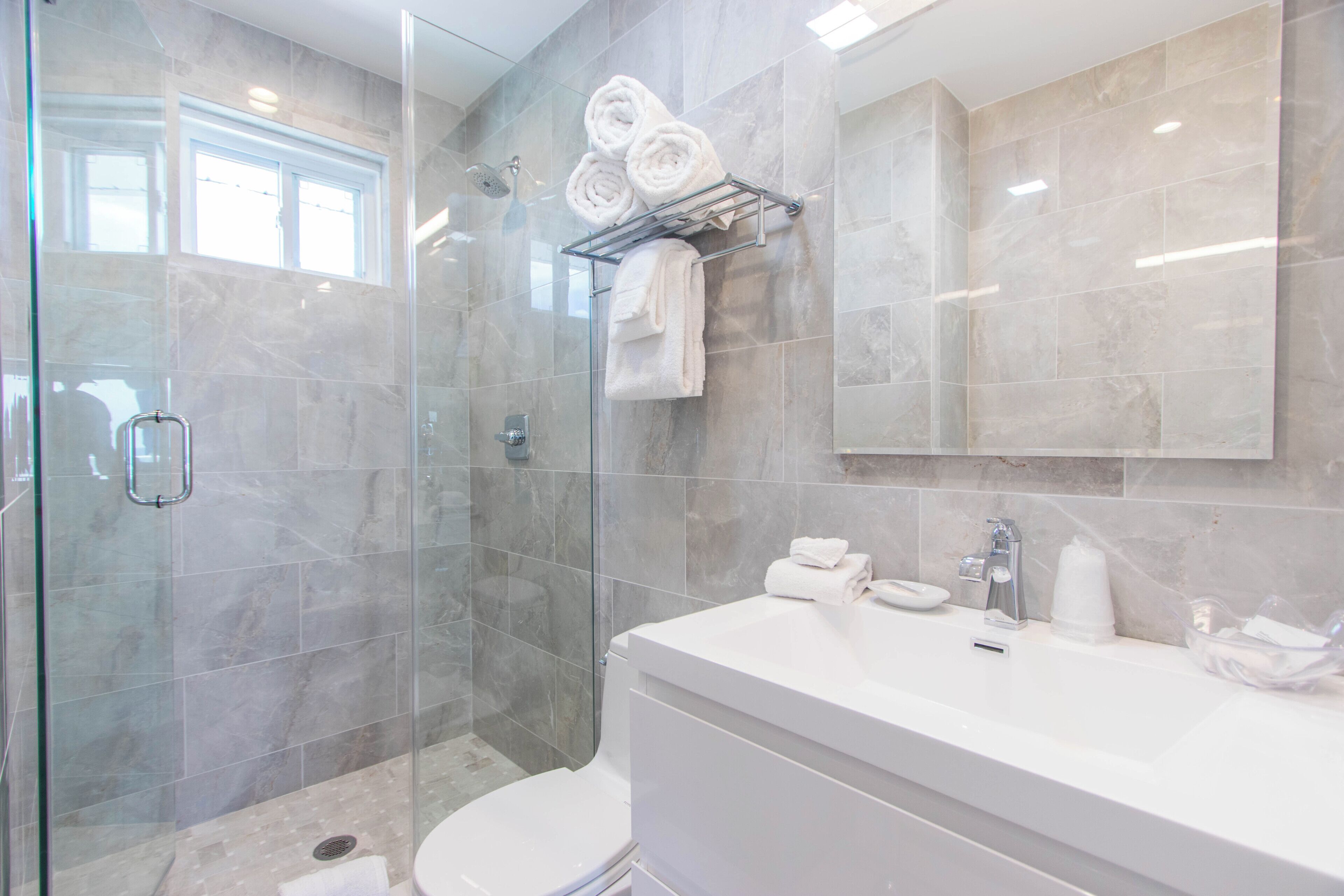 A modern bathroom with a glass-enclosed shower, a white sink, and a mirror above the vanity.