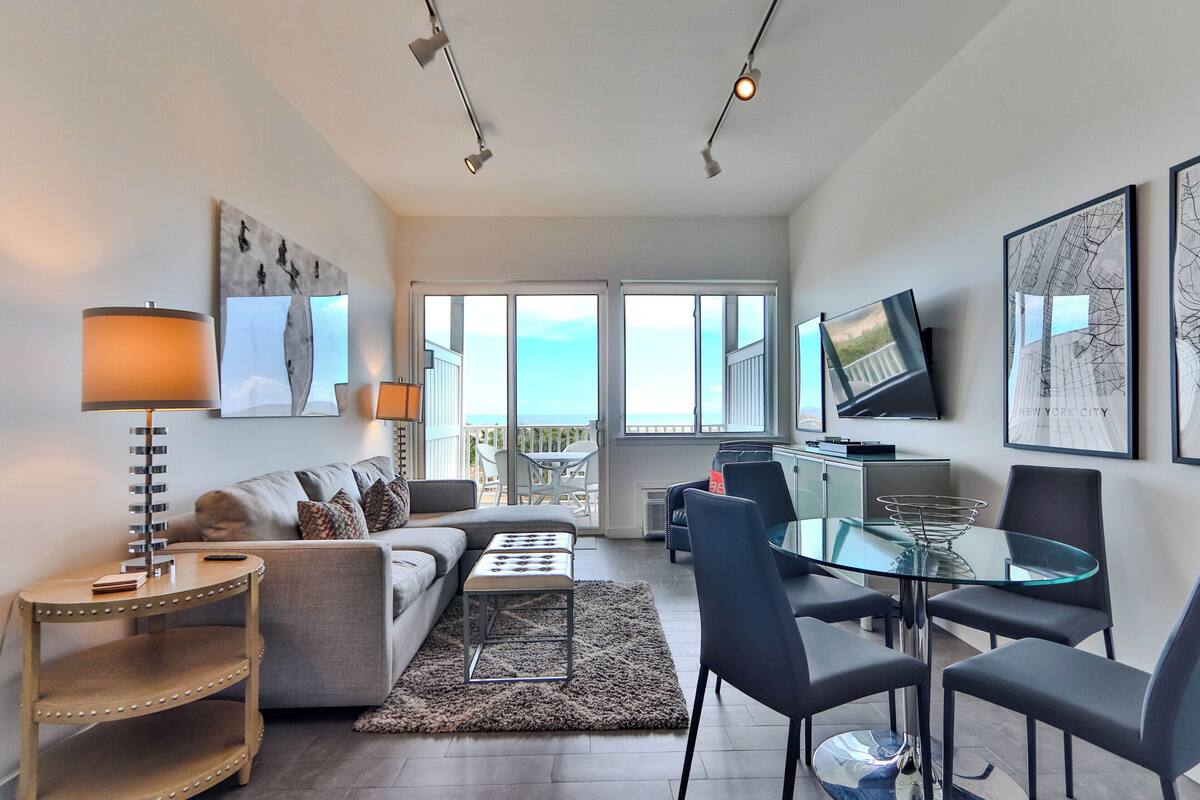 A modern living room with a sofa, a glass dining table, and a TV mounted on the wall.