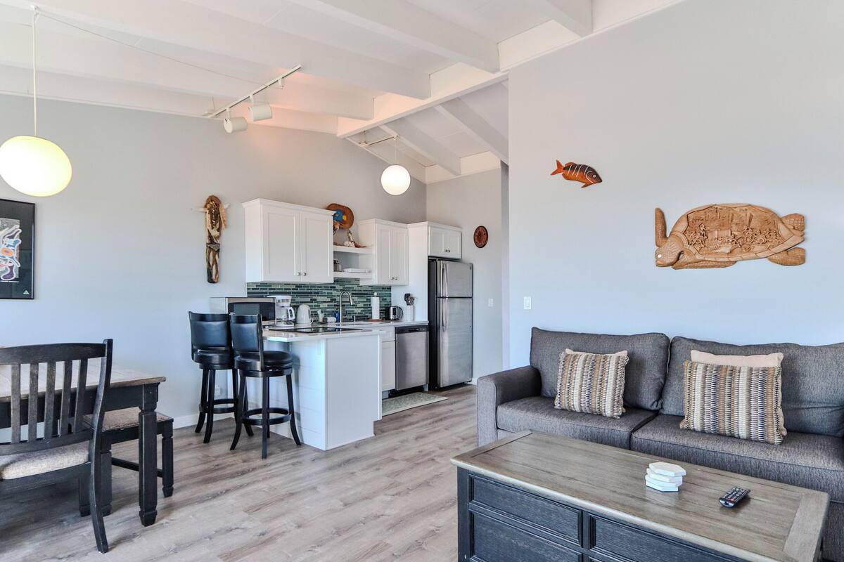A modern living space with a kitchen, dining area, and a sofa with decorative pillows.
