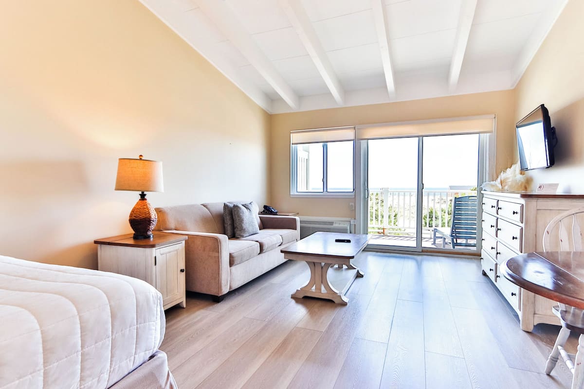 A room with a bed, a sofa, a coffee table, a TV, a dresser, and a balcony with a view.