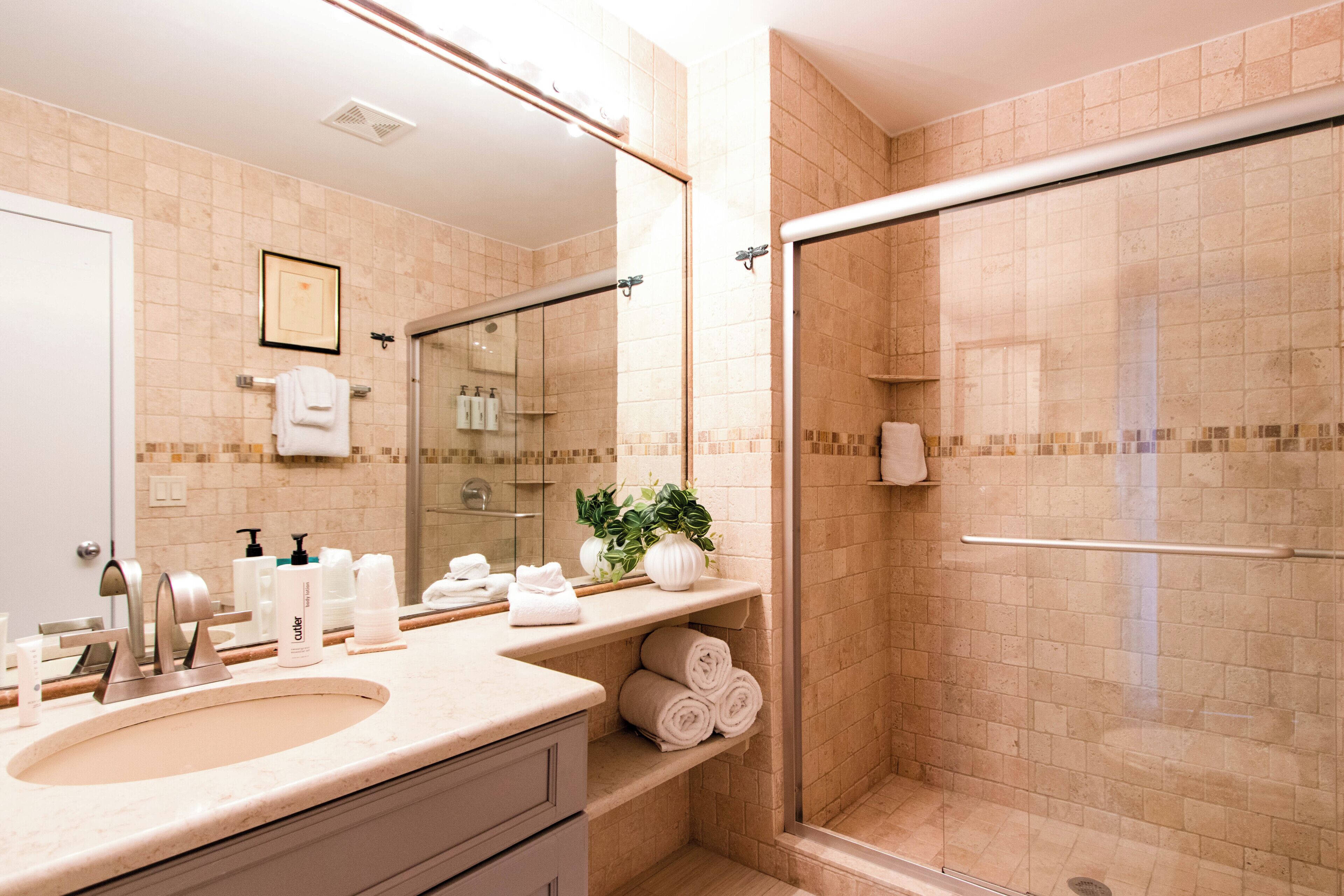 Bagno con lavandino, specchio, doccia e portasciugamani.
